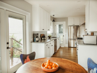 Hardwood floors, white cabinetry, light grey countertops, french doors to back deck. Natural wood round table with funky chairs with chicken images on them. Stainless steel appliances.