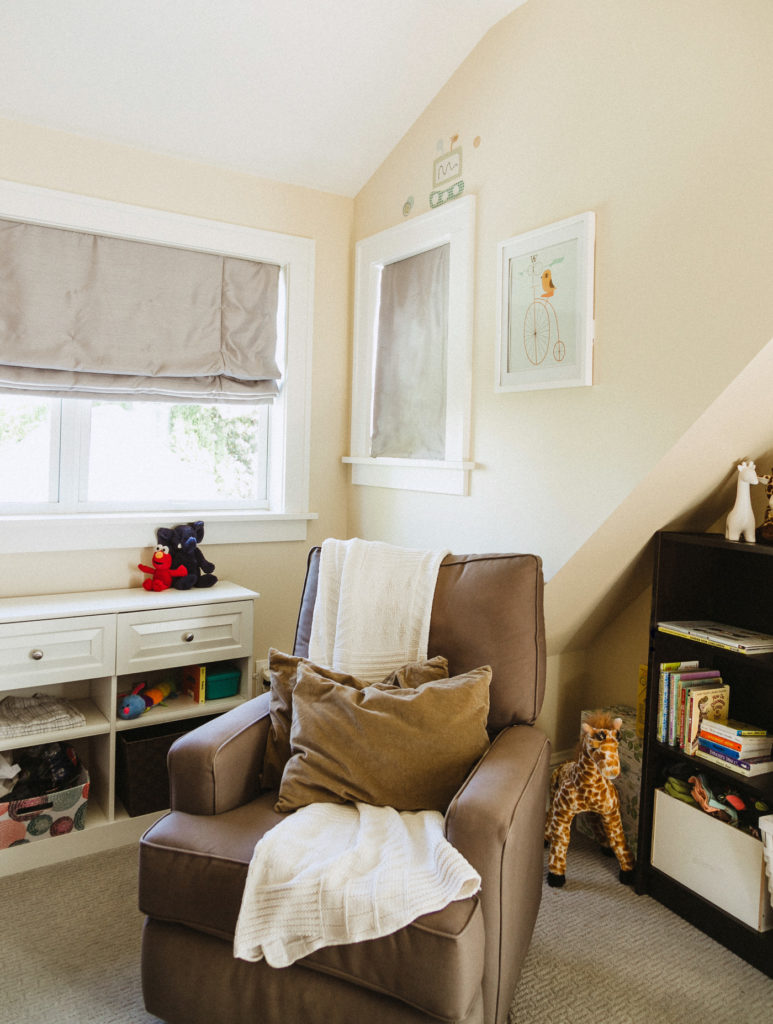 Storage bookshelves, corner view of comfy chair, roman shades on windows, vaulted ceiling.