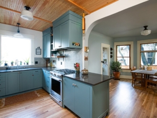 Teal cabinets, dark stone countertops, decorative tile backsplahs, wood floor, natural wood ceiling