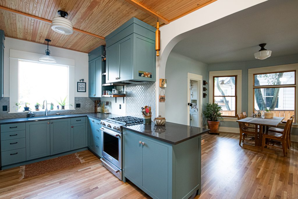 Teal cabinets, dark stone countertops, decorative tile backsplahs, wood floor, natural wood ceiling