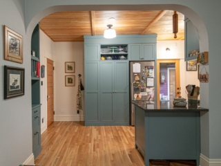 Wood floors and ceiling, full height pantry and refrigerator surround, teal cabinetry in a shaker style.
