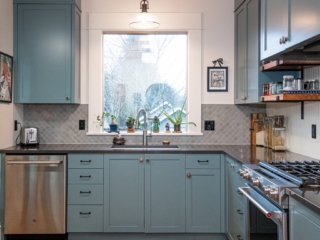 Teal cabinetry, oversized window, mid-tone grey scalloped tile. Undermount sink with pull-down faucet.