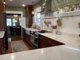 A galley style kitchen with William Morris inspired wallpaper, natural wood cabinets and brass accents.