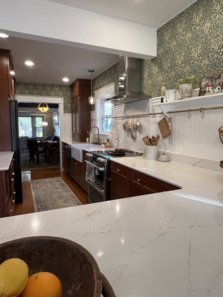 A galley style kitchen with William Morris inspired wallpaper, natural wood cabinets and brass accents.