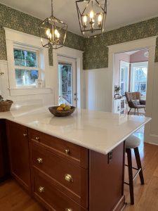 Kitchen peninsula with dark wood cabinetry, William Morris style wallpaper and home office beyond.