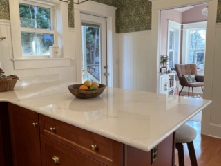 Kitchen peninsula with dark wood cabinetry, William Morris style wallpaper and home office beyond.