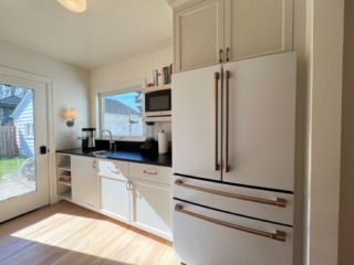 Light-filled room, cream cabinetry. White refrigerator with copper accents. Black countertop and backsplash.