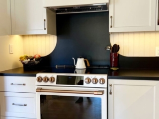 White slide-in range with copper accents and black custom backsplash.