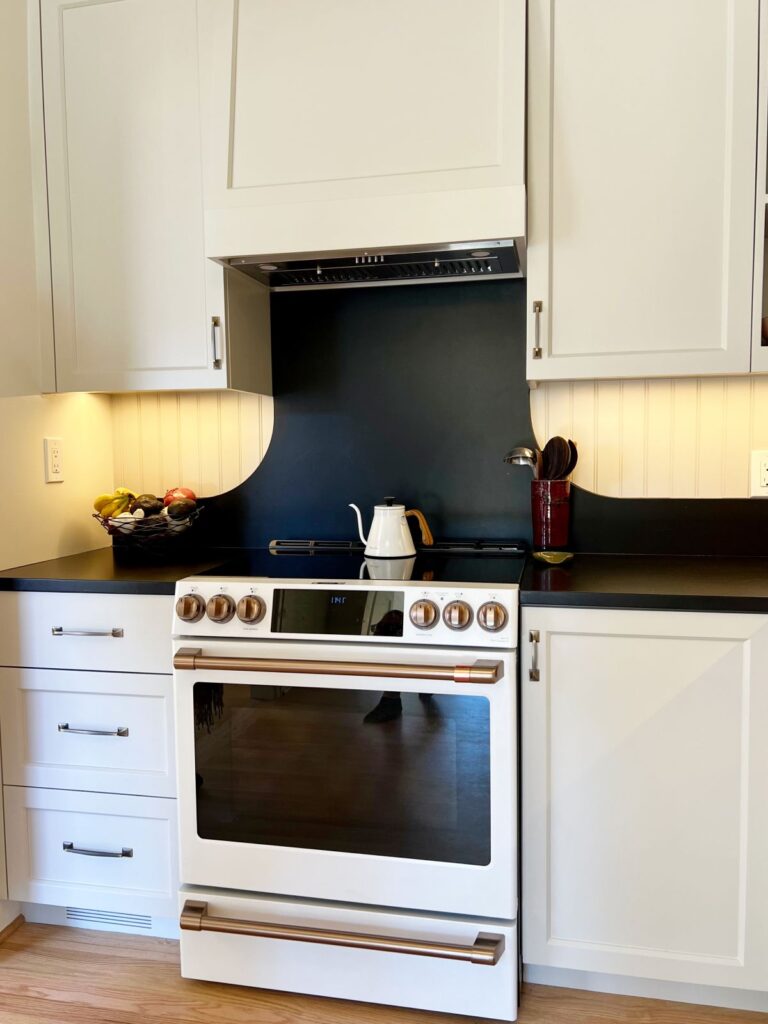 White slide-in range with copper accents and black custom backsplash.
