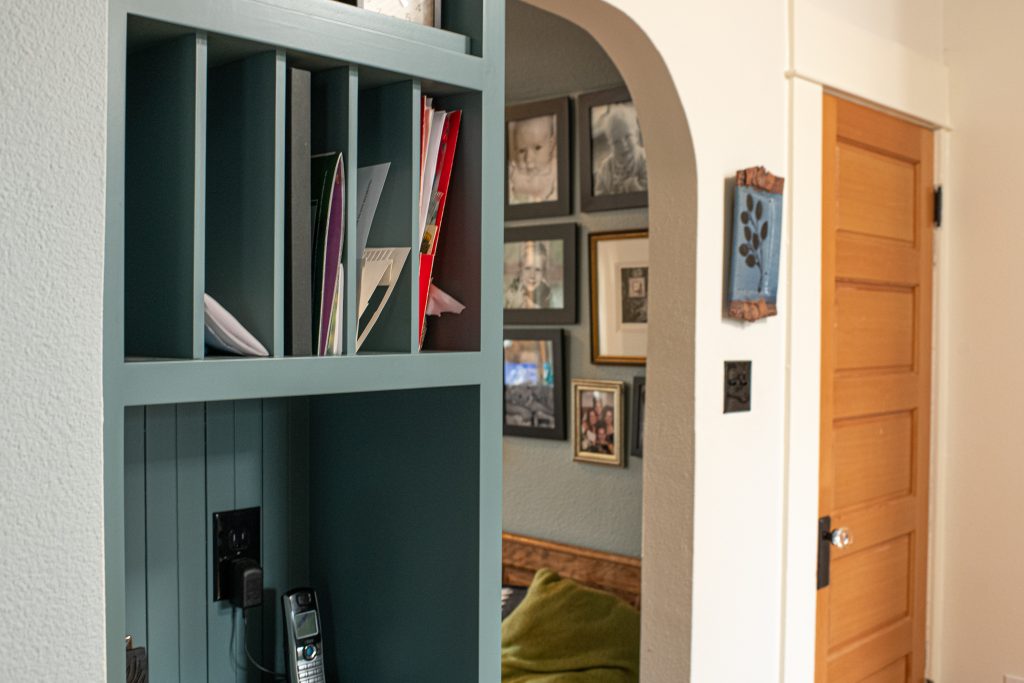 Mail sorting cubby shelves in custom, teal-painted cabinetry, above a little phone/charging zone.