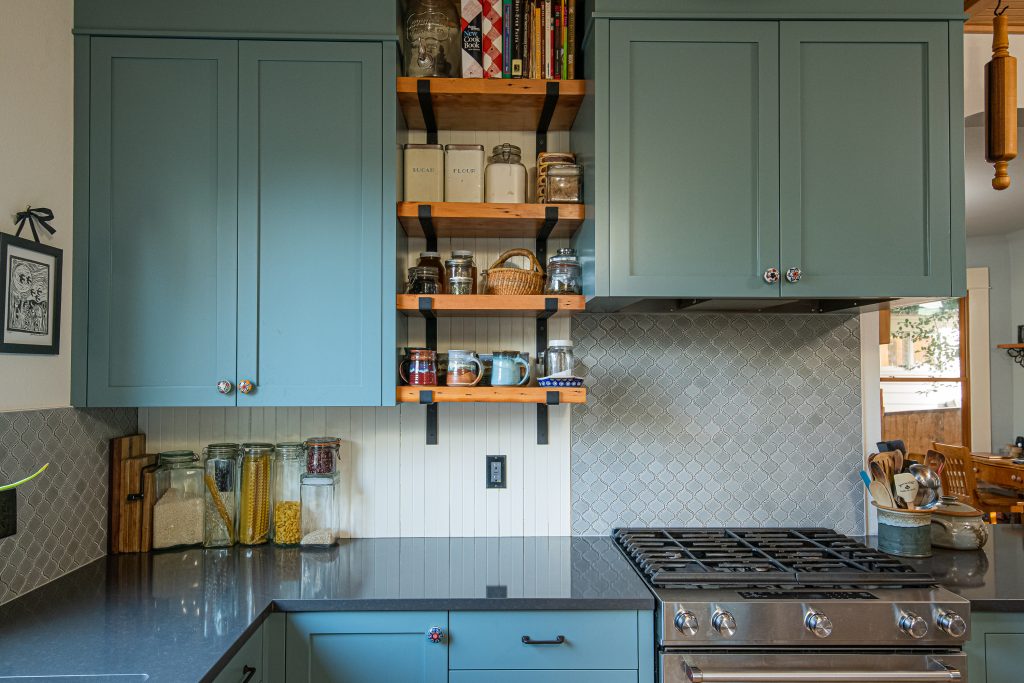 Teal painted cabinets, cream narrow wainscoting backsplash, spices and decorative accents on the open shelving.